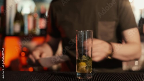 A professional bartender is preparing an alcoholic cocktail with ice cubes to customers at the bar or disco club.