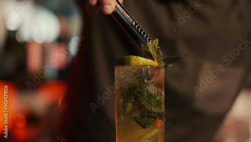 A professional bartender is preparing an alcoholic cocktail with ice cubes to customers at the bar or disco club.