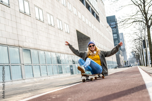 Athetic young woman riding longboard and sitting on it, urban background, yellow shirt and blue jeans, generation z female crazy lifestyle photo