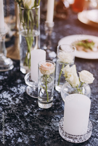 White candles in candelabra and white roses in glass vase on the wedding table decoration. 