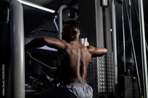 Shirtless african american man doing back exercises on a machine in the gym.