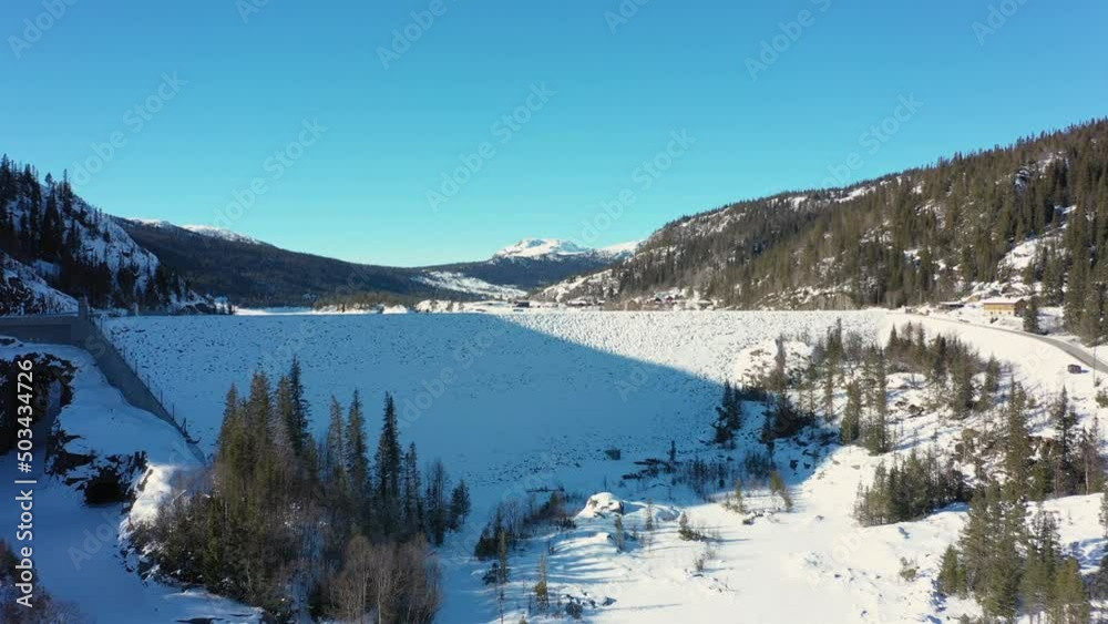 Tunhovd dam and water magazine - Aerial approaching snow covered dam from far to near with mountains and blue sky nature background - Statkraft dam for Nore hydroelectric powerplant Norway Tunhovd dam and water magazine - Aerial approaching snow covered dam from far to near with mountains and blue sky nature background - Statkraft dam for Nore hydroelectric powerplant Norway