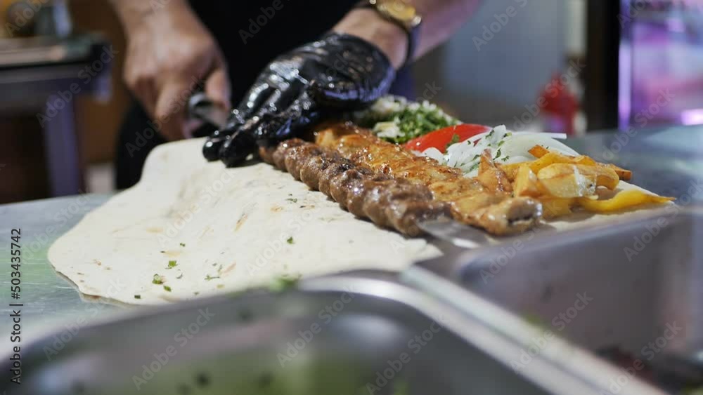 a restaurant shish kebab removes a kebab from a skewer on a thin pita bread with vegetables and fragrant greens cut into pieces. National Armenian food