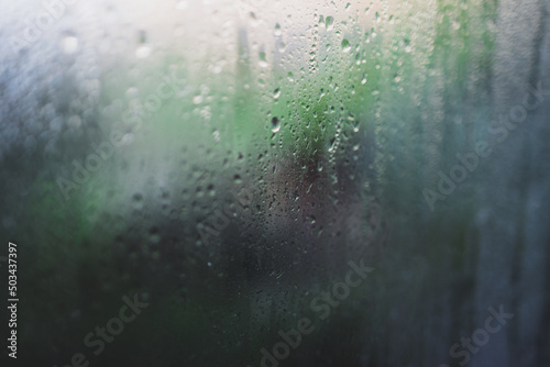 water droplets of humidity condensation on window glass seen from indoor with backyard bokeh in the background