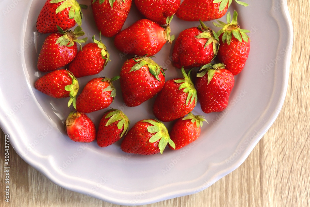 Lilac plate full of fresh strawberries on wooden table. Flat lay. Lilac plate full of fresh strawberries on wooden table. Flat lay.