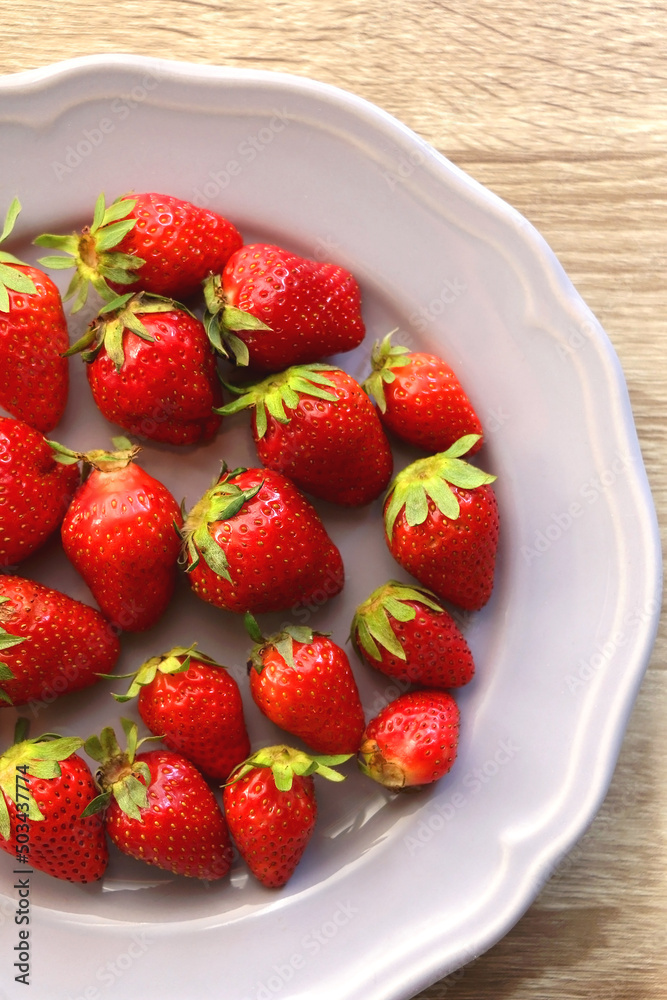 Lilac plate full of fresh strawberries on wooden table. Flat lay. Lilac plate full of fresh strawberries on wooden table. Flat lay.