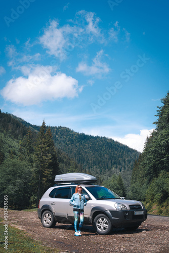 Girl standing near suv car at the Charpatians mountain. Vertical photo. summer day. Road trip, vacation and travel concept. Roff rack box. © Sergey