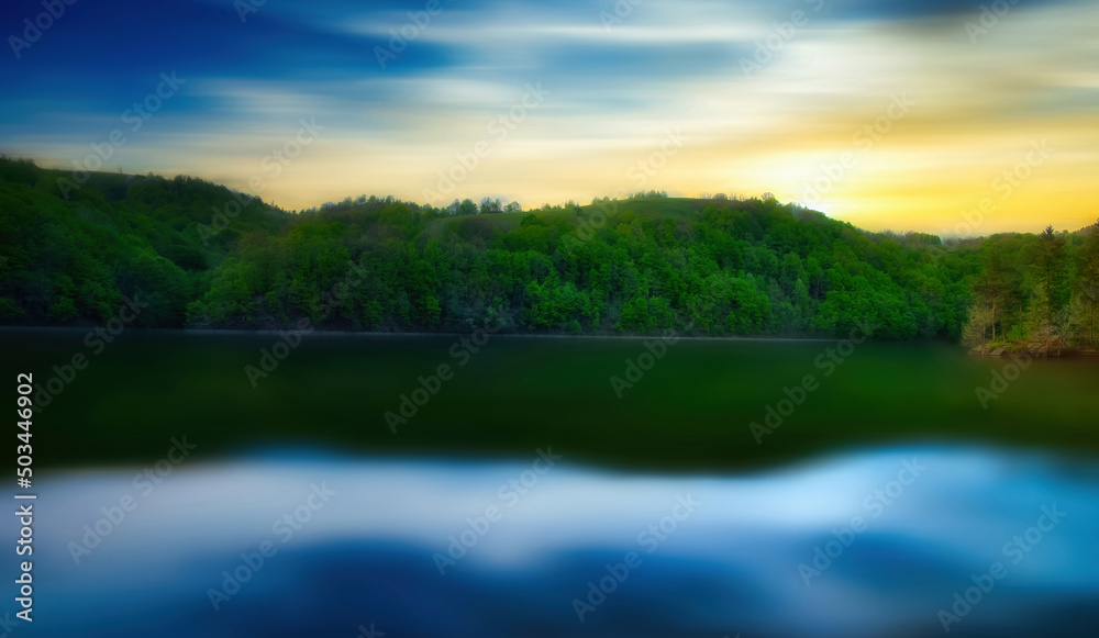 Obraz premium A lake with a long exposure time, with the reflection of the clouds in the water at sunset