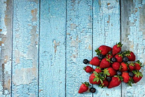 zenithal view of a rustic travel table, blue with red fruits, strawberries and blueberries, copy space. Back Ground