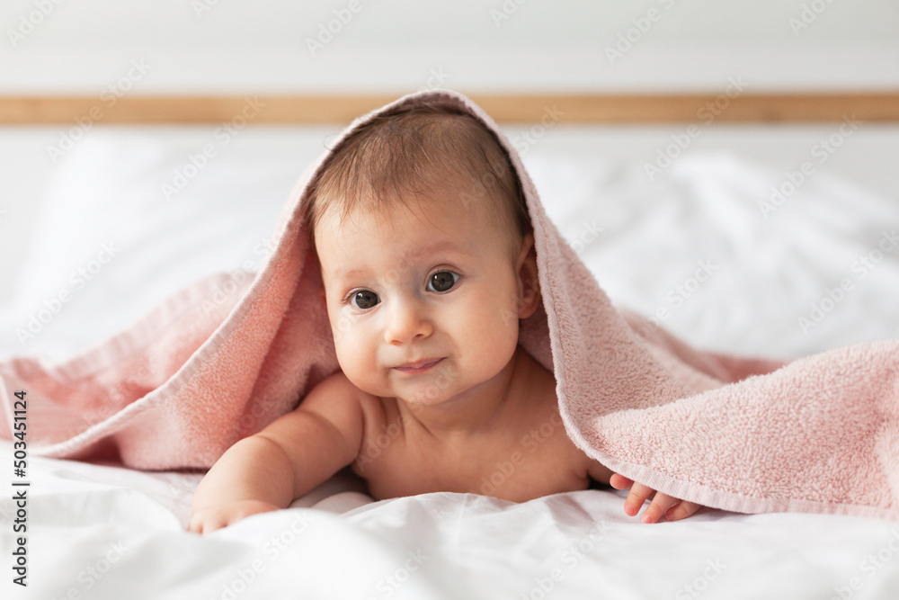 Happy laughing baby wearing pink hooded towel on parents bed after bath or shower.