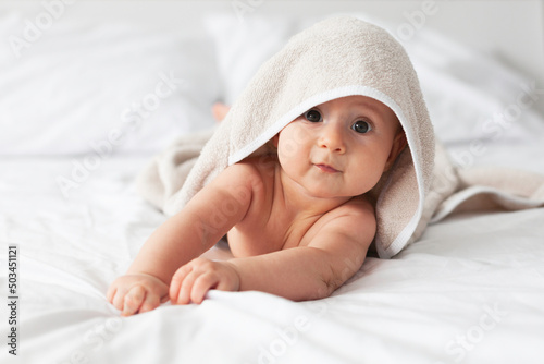 Happy laughing baby wearing biege towel on parents bed after bath or shower.