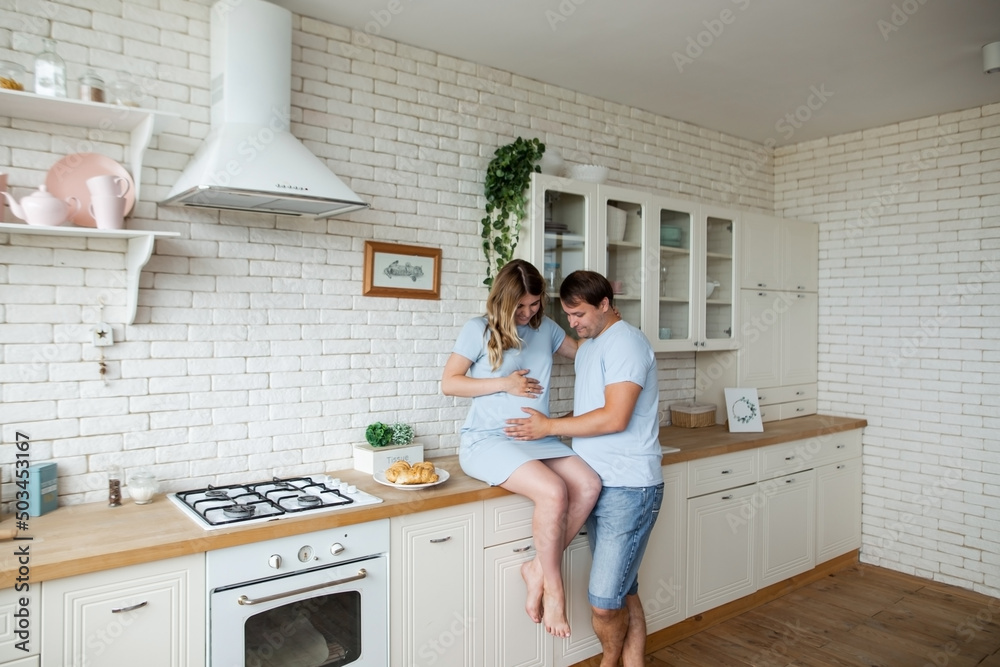 pregnant woman and her handsome husband embracing and smiling while spending time together near window at home. Romantic couple expecting new baby indoors. Parenthood concept pregnant woman and her handsome husband embracing and smiling while spending time together near window at home. Romantic couple expecting new baby indoors. Parenthood concept