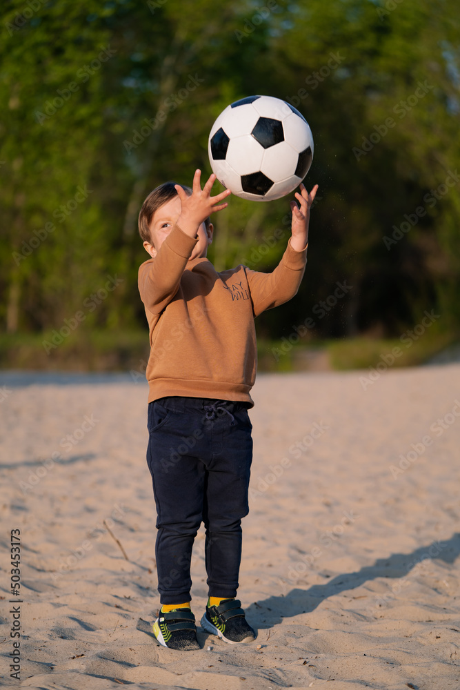 Kid Throws Ball Up with His Hands. Funny Little Boy Playing with Black and White Soccer Ball in Park on Sand Kid Throws Ball Up with His Hands. Funny Little Boy Playing with Black and White Soccer Ball in Park on Sand
