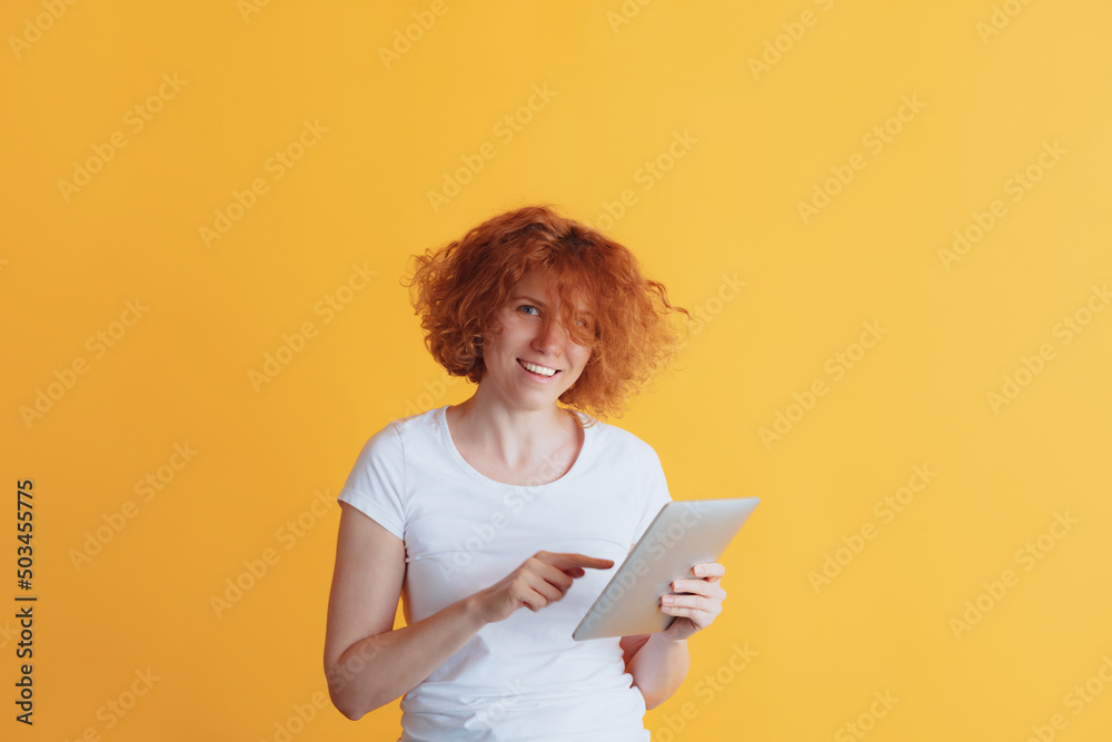 Portrait of smiling woman typing message on tablet or searching information isolated over yellow studio background Portrait of smiling woman typing message on tablet or searching information isolated over yellow studio background