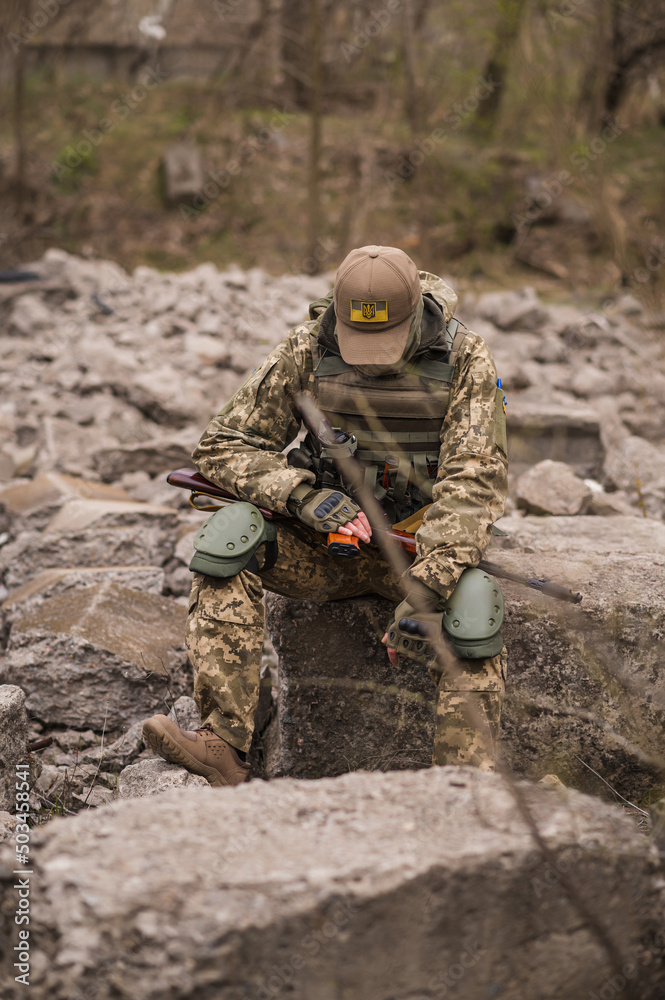 Soldier of the Armed Forces of Ukraine. A military man in tactical uniforms and with a machine gun in his hands sits on a stone