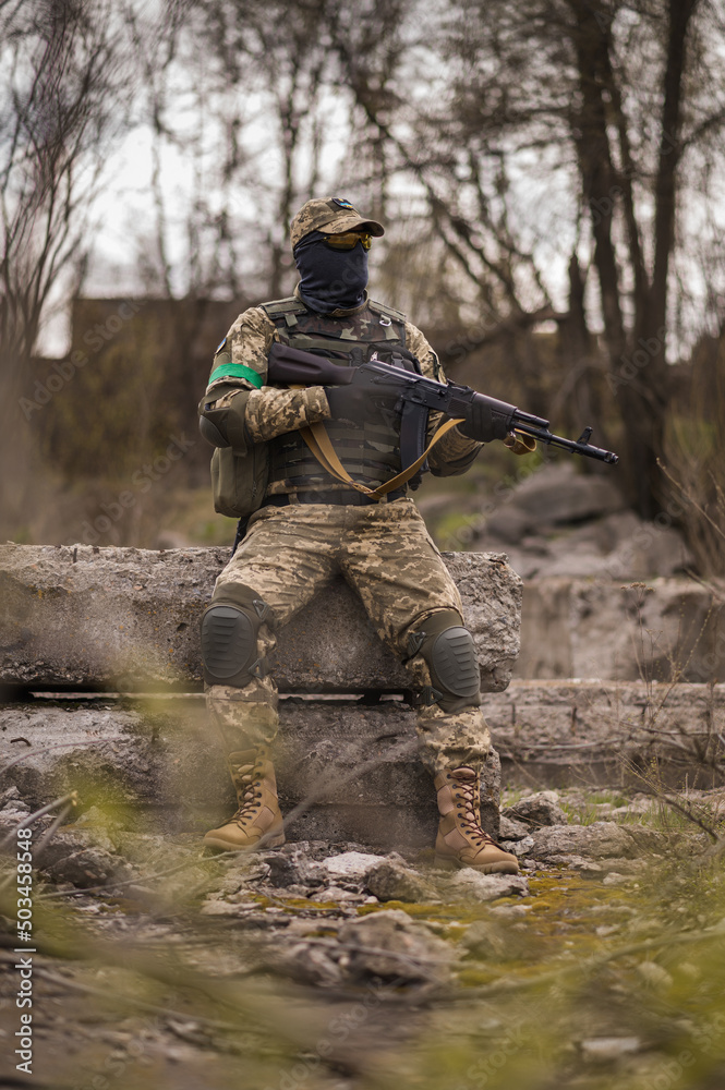 Soldier of the Armed Forces of Ukraine. A military man in tactical uniforms and with a machine gun in his hands sits on a stone