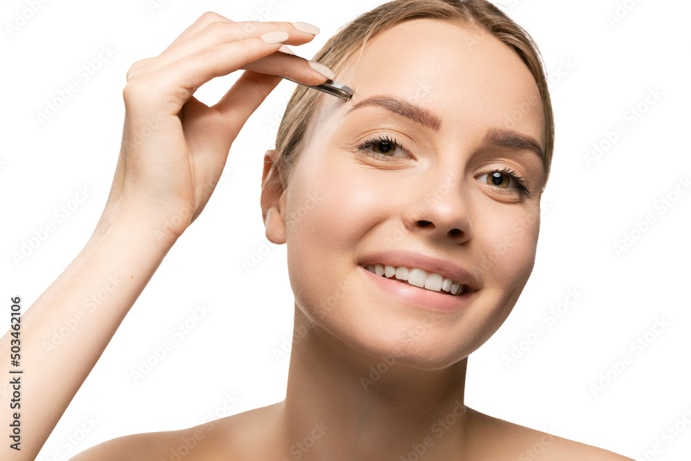 Close up beautiful young smiling woman tweezes eyebrows isolated on white background. Concept of cosmetics, makeup, natural beauty