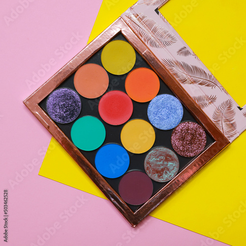 Colorful eyeshadow makeup palette. Realistic image with matte, glitter, multichrome pigments. Shadows set in vibrant colorful scheme. Top view flat lay package isolated on colorful background. photo