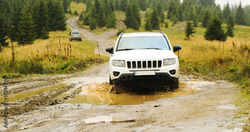 white SUV, driving through a stupid puddle in the forest in the mountains. Front view, car travel in Carpathians, Ukraine, Europe