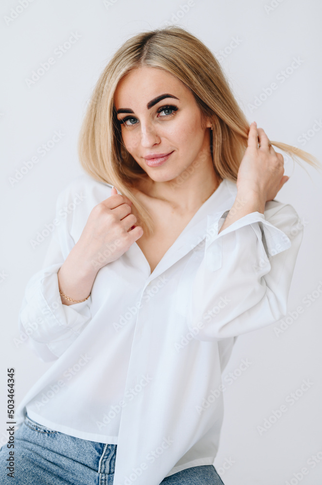 Blonde girl smiles sweetly while straightening her hair on a white background.