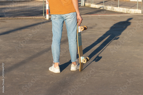 Cropped view of young man holding a long board on his hands wearing an alternative street style outfit