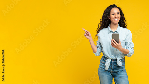 Excited woman pointing aside at copy space using cell
