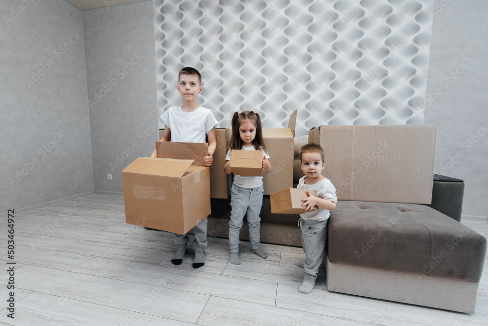 Brothers and sister are playing and enjoying moving to a new apartment against the background of cardboard boxes and a sofa. Purchase of real estate. Housewarming, delivery. Brothers and sister are playing and enjoying moving to a new apartment against the background of cardboard boxes and a sofa. Purchase of real estate. Housewarming, delivery.