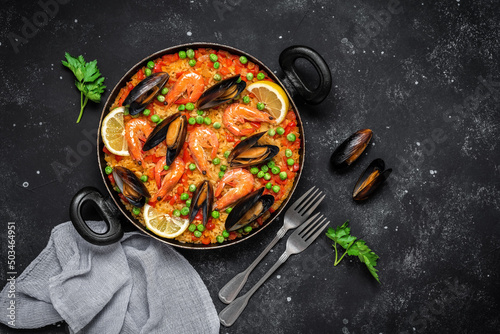 Traditional Spanish paella with seafood in a frying pan on a black stone grunge background. Top view, flat lay. Mediterranean food.
