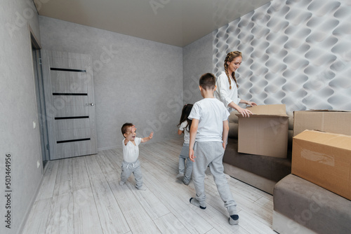 A young mother with children unpacks a box of things after moving to a new apartment. Purchase of real estate. Housewarming, delivery and transportation of goods. © Andrii