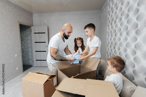 A young father with children unpacks a box of things after moving to a new apartment. Purchase of real estate. Housewarming, delivery and transportation of goods.