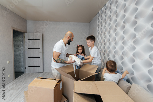 A young father with children unpacks a box of things after moving to a new apartment. Purchase of real estate. Housewarming, delivery and transportation of goods. © Andrii