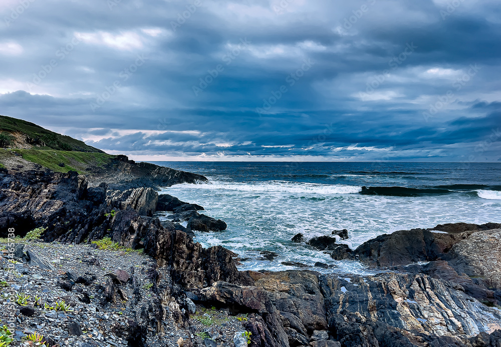 Landscape view of an interesting complex rocky, coastal headland and a surf scene with dark, ominous storm clouds out to sea forming a background to this moody image.