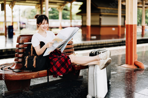 summer  relax  vacation  travel  portrait of a cute Asian girl looking at a map to plan a trip while waiting at the train station.