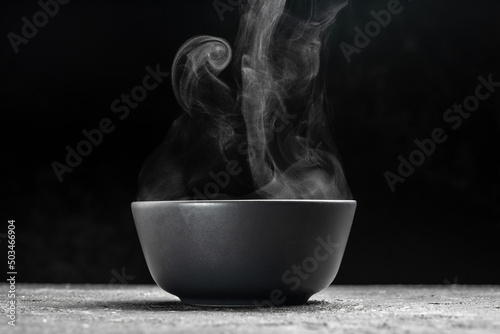 Bowl of hot steam of hot soup with smoke. black ceramic bowl on dark background. Hot food. Culinary, cooking, concept