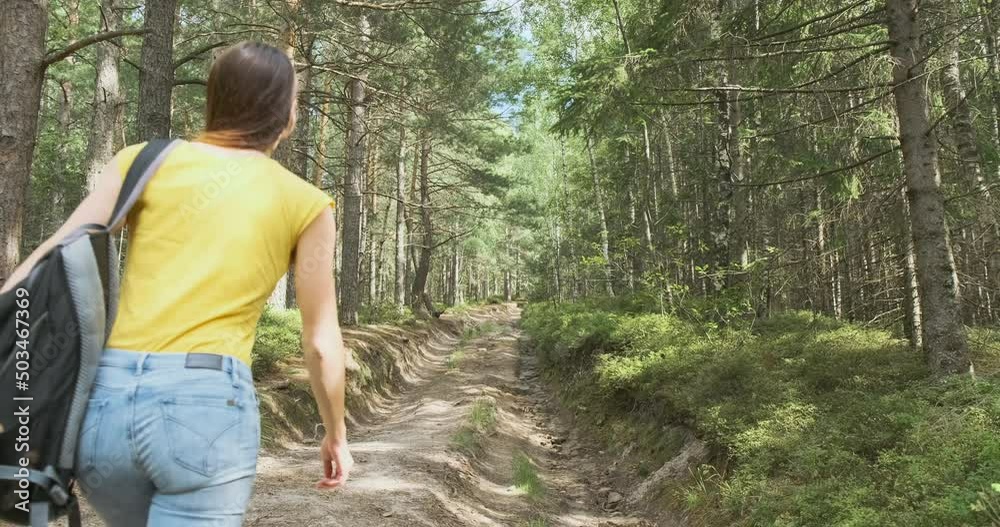 Young woman climbing up a forest path with a backpack. Walk in the fresh air among wild coniferous trees Young woman climbing up a forest path with a backpack. Walk in the fresh air among wild coniferous trees