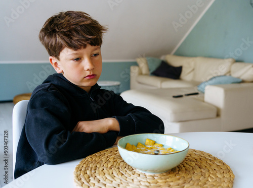 The boy sits over the plate and does not want to have a breakfast. No appetite. 