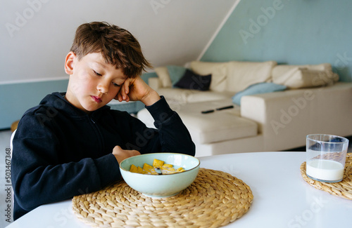 The boy sits over the plate and does not want to have a breakfast. No appetite. 