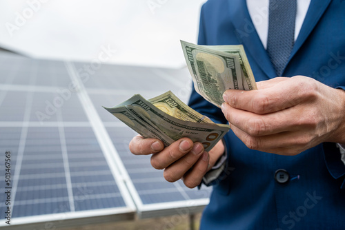  hands holding a round sum of bank new dollars on a background of new solar panels.