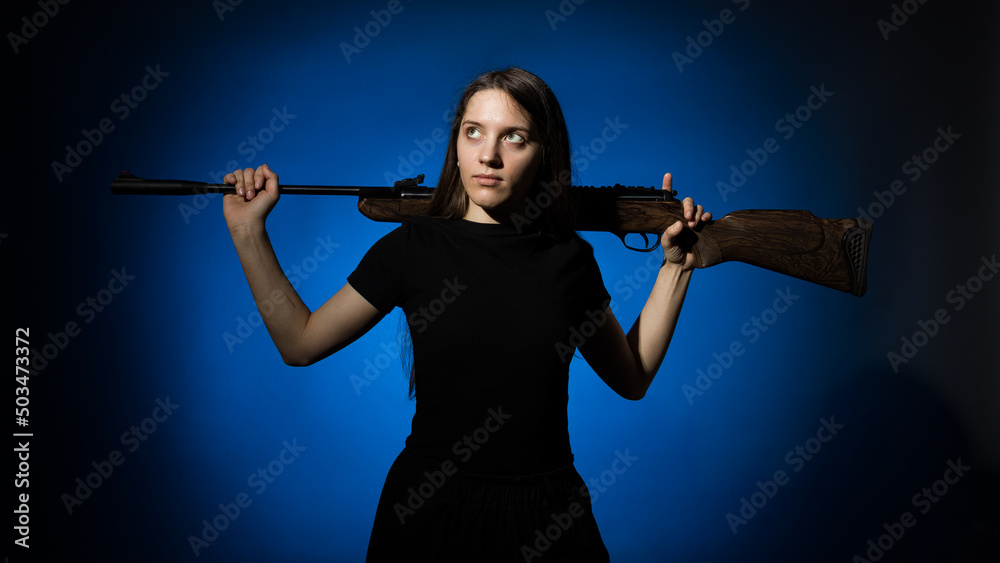 young beautiful woman with long hair in a black t-shirt holds a gun on her shoulders on a blue background young beautiful woman with long hair in a black t-shirt holds a gun on her shoulders on a blue background