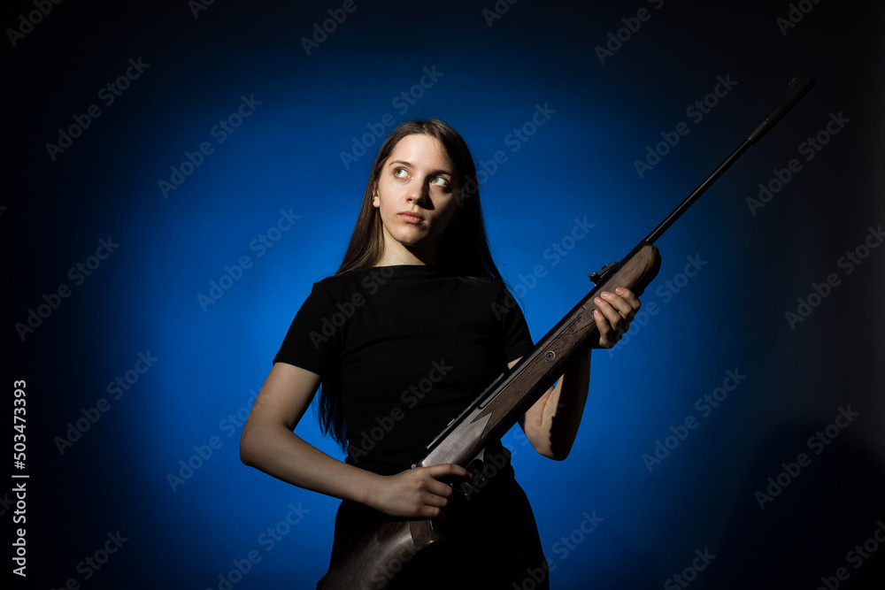 young beautiful woman with long hair in a black t-shirt holding a gun on a blue background young beautiful woman with long hair in a black t-shirt holding a gun on a blue background