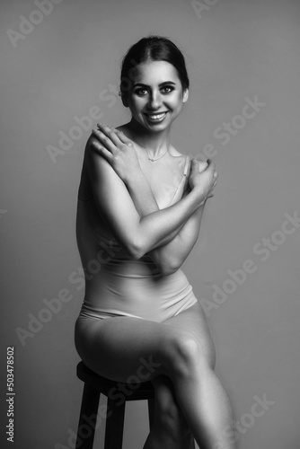 Beauty Ballerina in a swimsuit sit on wooden chair on a gray background