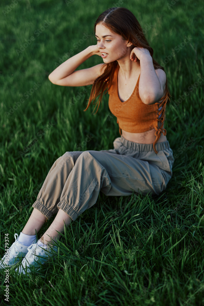 A beautiful redheaded woman sits on the green grass in a garden and looks out into the distance at a sunset surrounded by blooming nature A beautiful redheaded woman sits on the green grass in a garden and looks out into the distance at a sunset surrounded by blooming nature