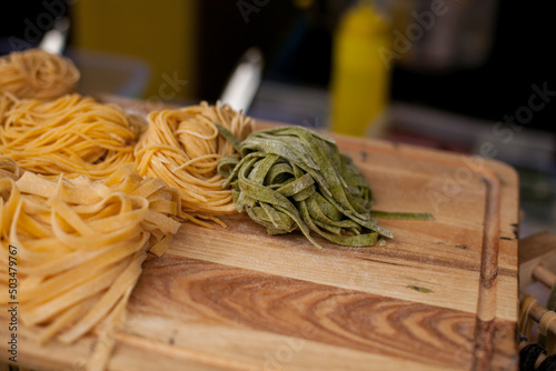 Egg noodles of different colors on a wooden board. Row of three small different colored bundles of wheat ribbon pasta strips on wood grain table background. street food.