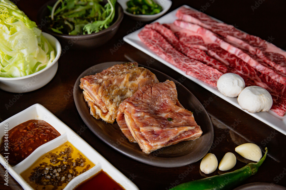 Korean Grilled BBQ combo with wagyu and marinated beef set on the traditional grill table, with lettuce, dipping sauce and pickle dishes Korean Grilled BBQ combo with wagyu and marinated beef set on the traditional grill table, with lettuce, dipping sauce and pickle dishes