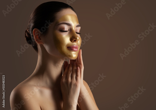 Facial peeling Golden Mask. Woman with Gold Lifting Face Mask over Dark Background. Beauty Model enjoying Skin Care Spa Cosmetology with closed Eyes. Women Anti Aging Cosmetics photo