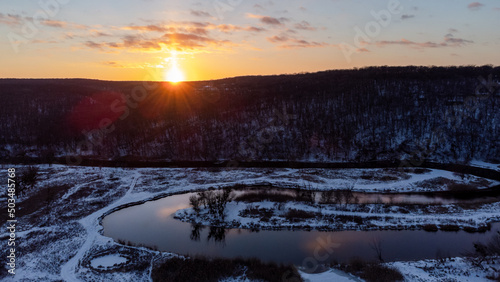 Winter aerial panorama view on snowy river curve with scenic reflection. Zmiyevsky region on Siverskyi Donets River in Ukraine. Sunset sun shining above woody hill