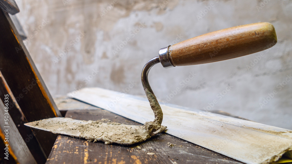 Close-up of a dirty trowel against a wall with plaster. Wall renovation process. Renovation concepts. Close-up of a dirty trowel against a wall with plaster. Wall renovation process. Renovation concepts.