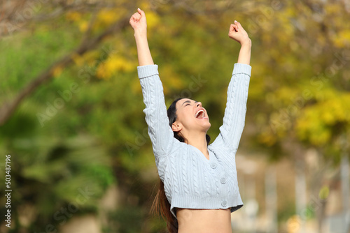 Excited woman raising arms in a park celebrating good day
