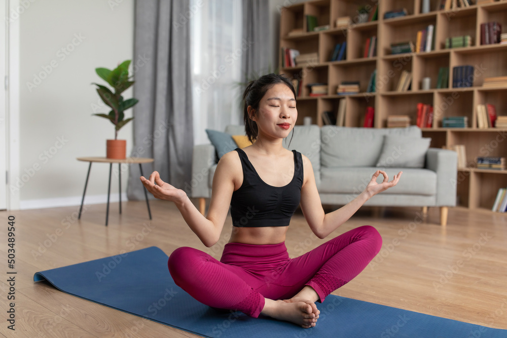 Peaceful korean lady in sportswear sitting on yoga mat with closed eyes, meditating alone at home, free space Peaceful korean lady in sportswear sitting on yoga mat with closed eyes, meditating alone at home, free space