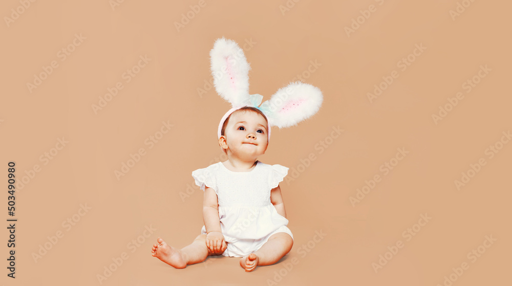 Portrait of cute baby with rabbit ears sitting on brown background